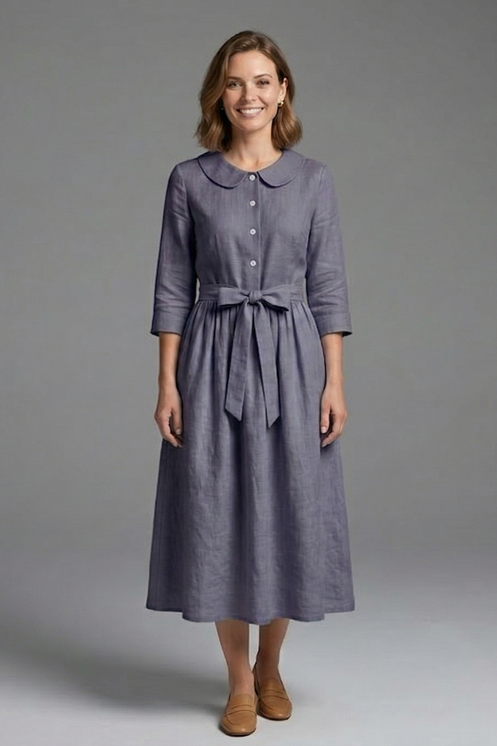 Woman showing waist tie detail gray dress on plain gray background.