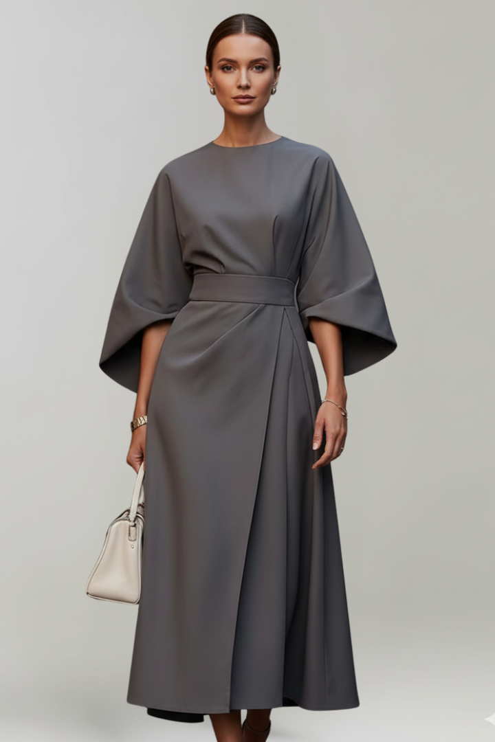 Female model posing in long midi dress, studio gray background.