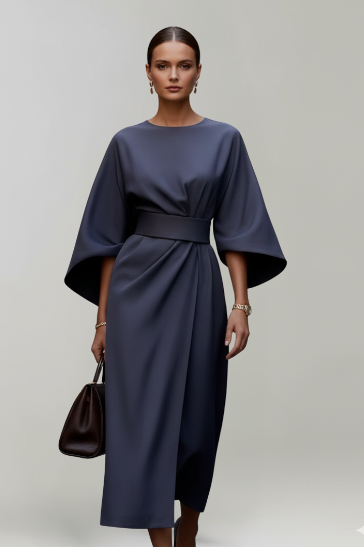 A woman wears a belted midi dress on plain gray background.