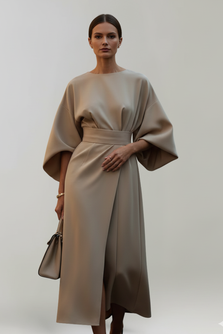 Female model wearing modest dress with wide sleeves, gray background.