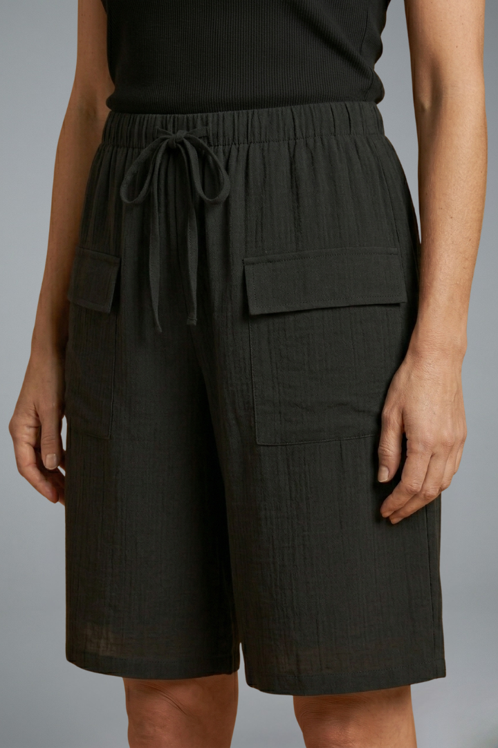 Model wearing pocket shorts, relaxed stance, plain gray background