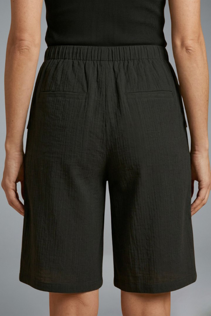 Model in regular fit black shorts, back angle, gray background.