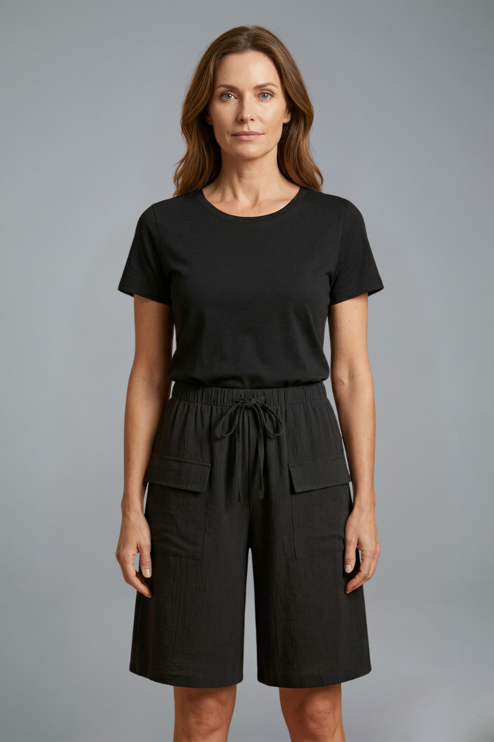 Woman wearing casual black shorts and top, front view, plain gray background.