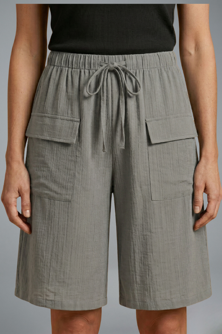 Woman wearing casual shorts, front pose, plain gray background setting.