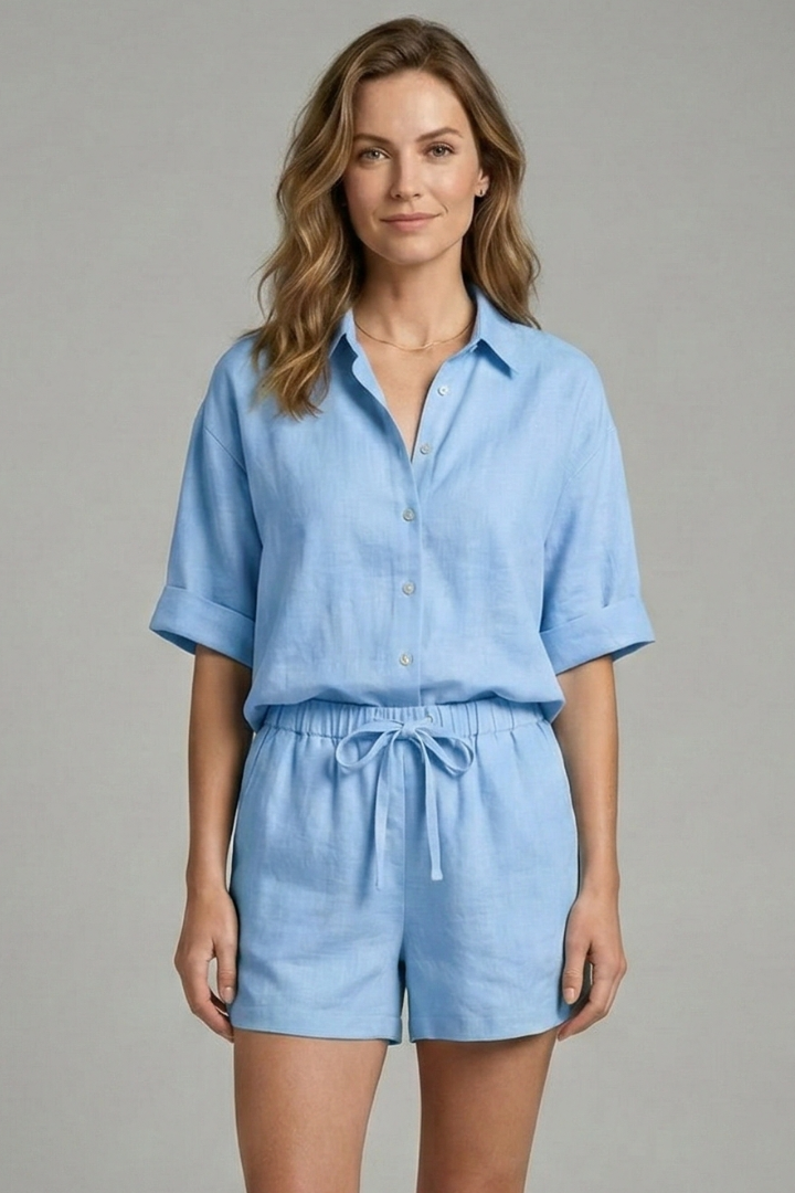 Female model wearing buttoned blue shirt with wide-leg shorts, gray background.