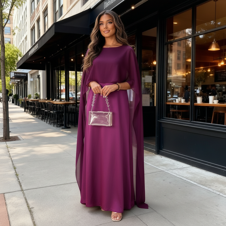 Female wearing a long formal gown with elegant cape styling on a plain background.