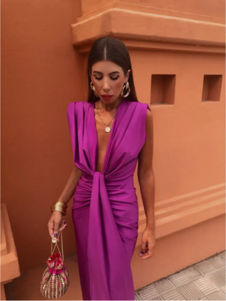 Female model posing in a sleeveless long dress with sculpted ruching on a plain background.