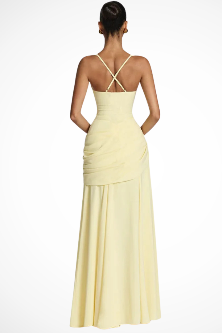 Woman posing in a floor-length evening dress with gathered fabric and wide straps on a plain background.