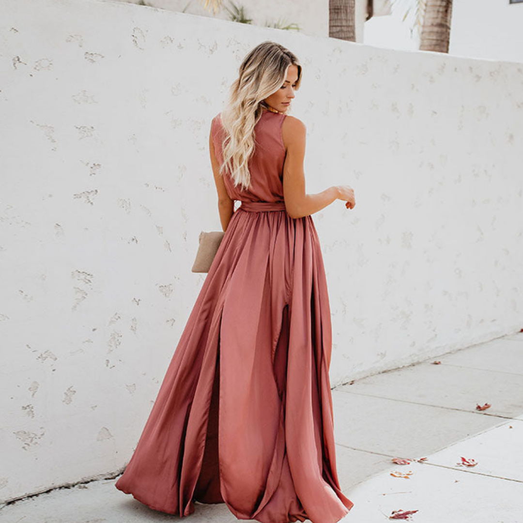 Female model showcasing a long flowing dress with sleeveless design on a plain background.