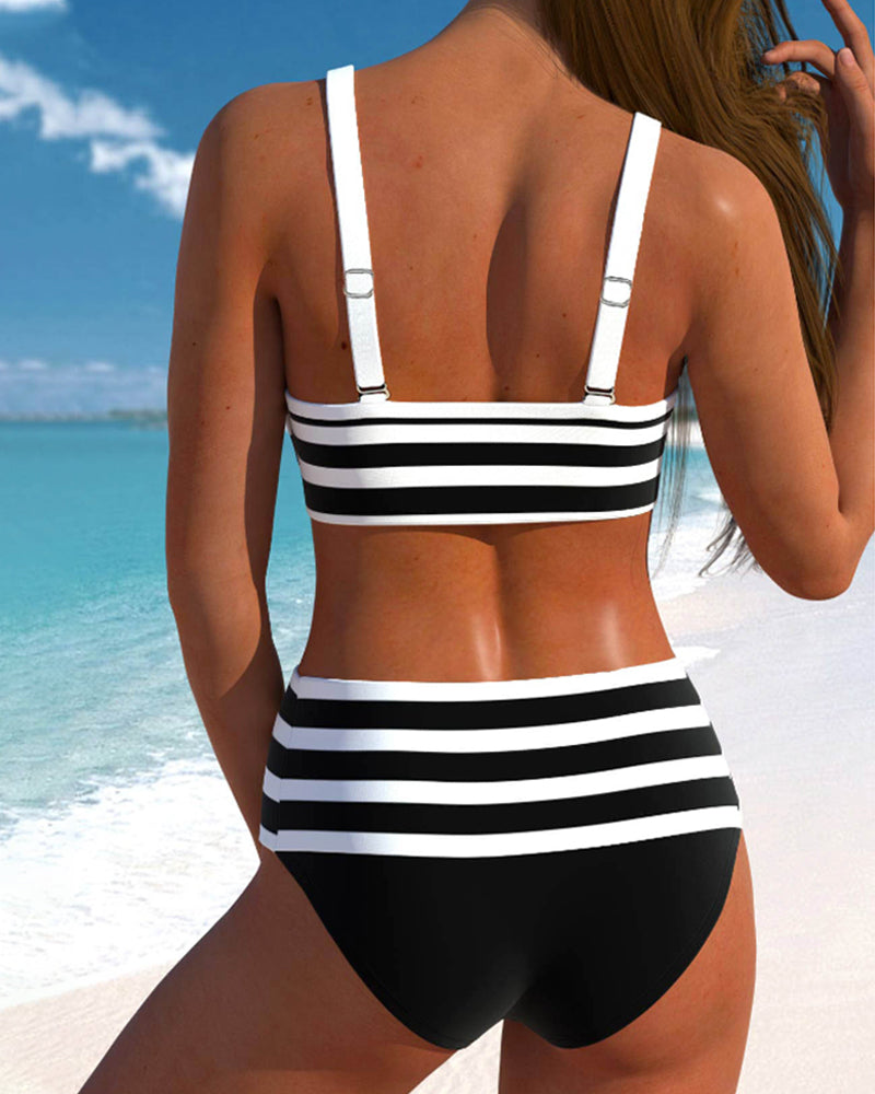 Woman in striped two-piece swimwear standing by a beach background, back angle