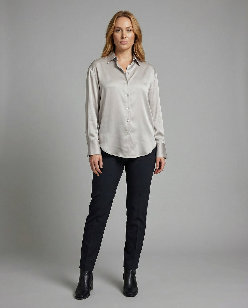 Female model in an elegant silk blouse with refined detailing on a plain background.
