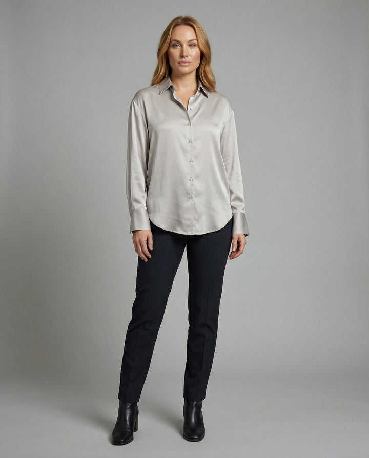 Female model in an elegant silk blouse with refined detailing on a plain background.