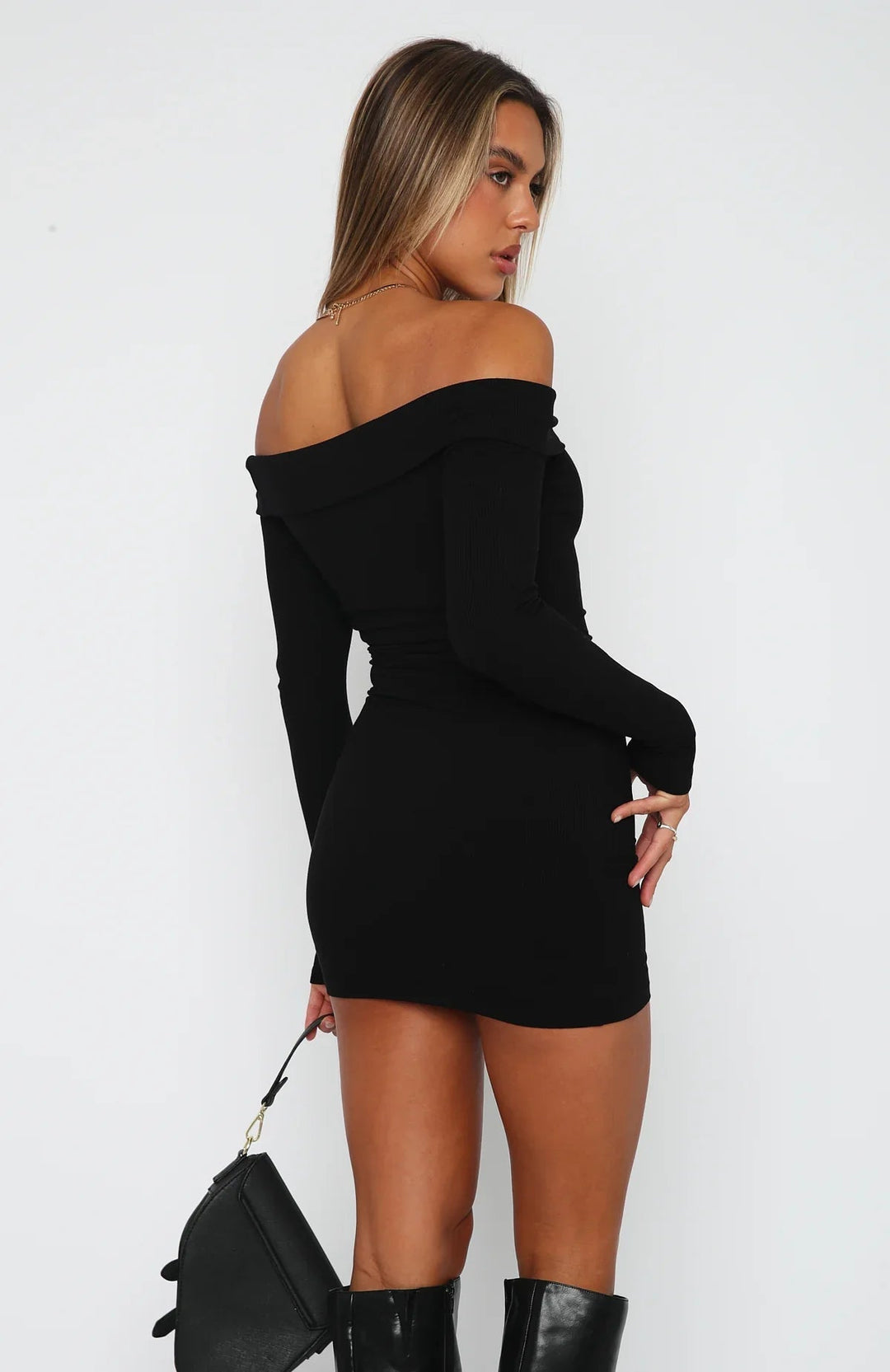 Woman in a fitted off shoulder mini dress with long sleeves on a plain background.