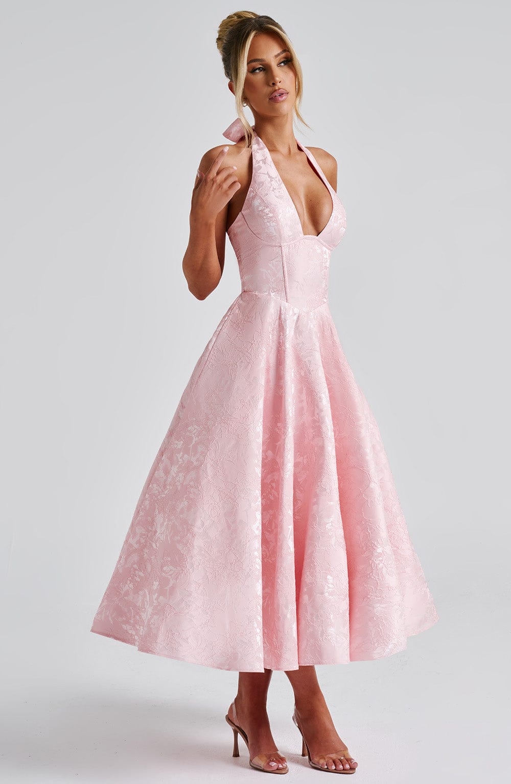 Woman in an elegant halter midi dress styled for a wedding guest outfit on a plain background.
