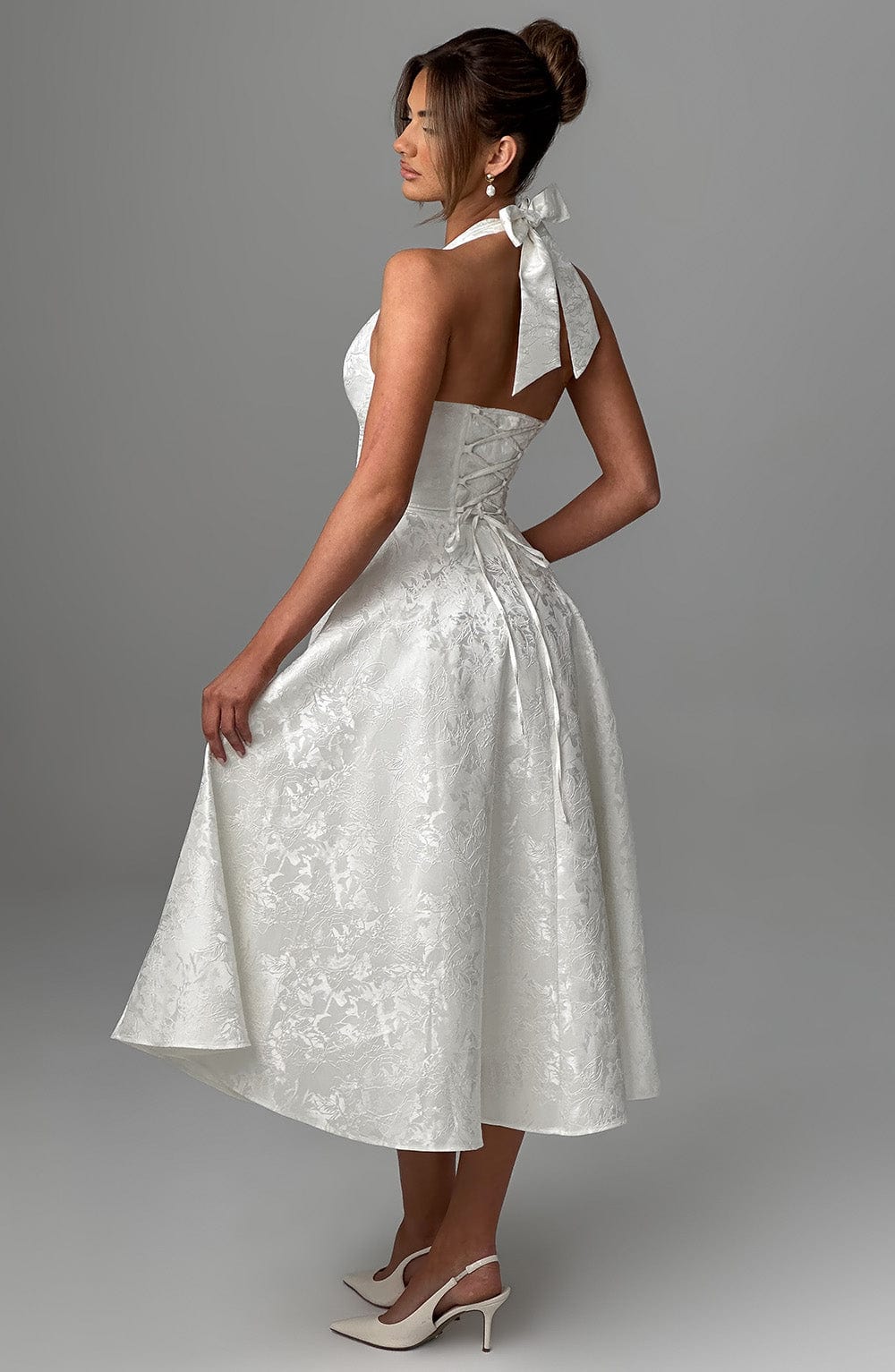Female model in a midi-length halter dress photographed against a plain backdrop.