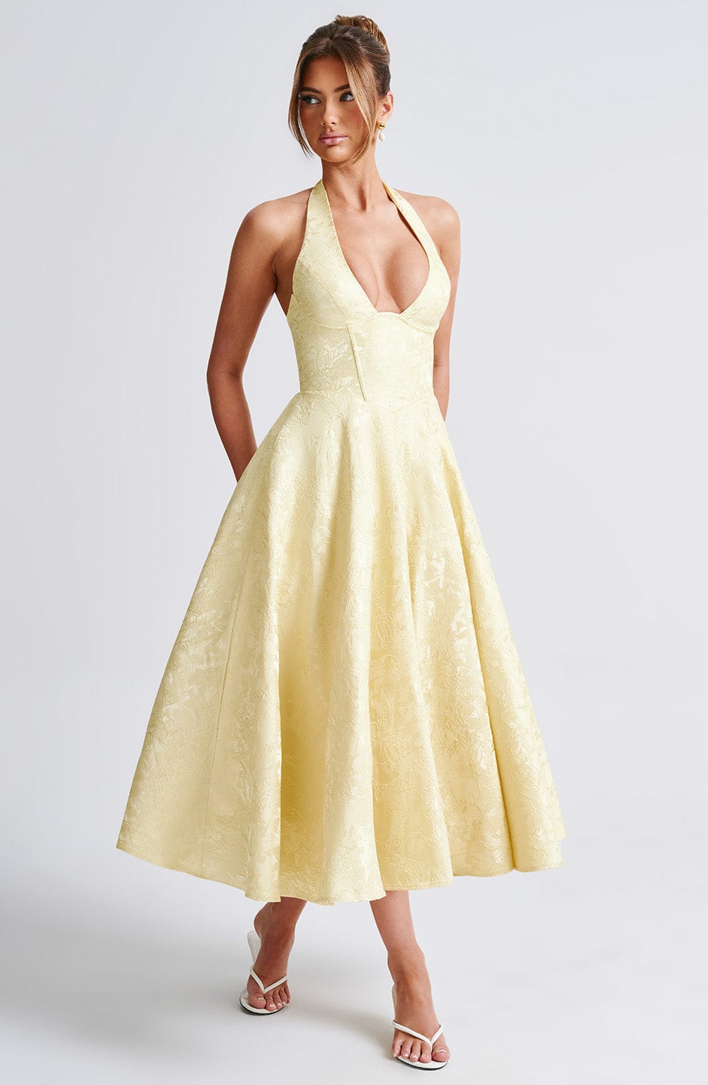 Female model wearing a sleeveless occasion dress with a halter neckline on a plain background.
