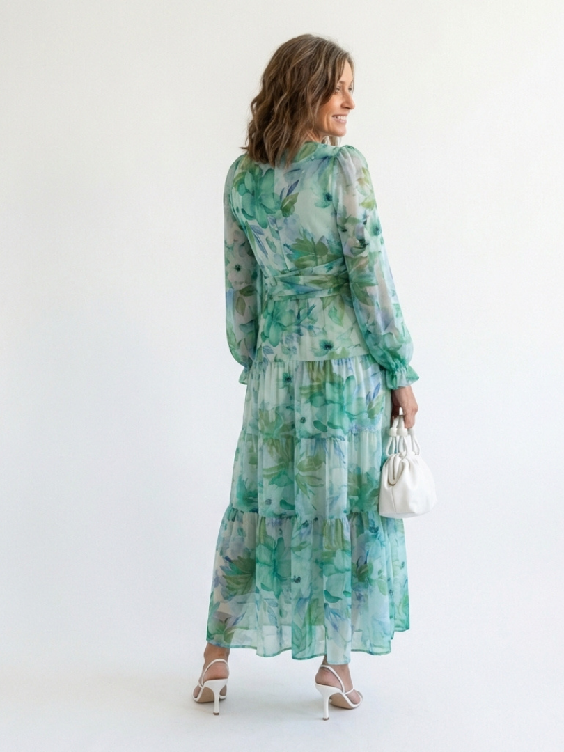 Woman in a long sleeve floral maxi dress with a v neckline on a plain background.