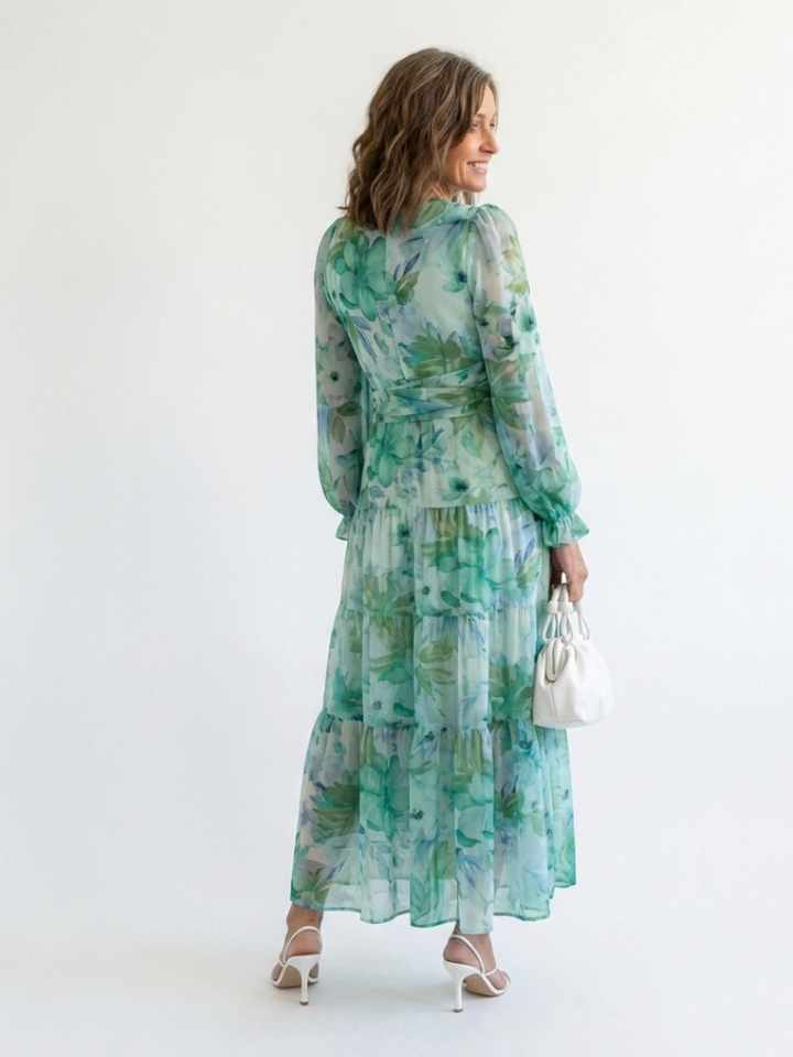 Woman in a long sleeve floral maxi dress with a v neckline on a plain background.