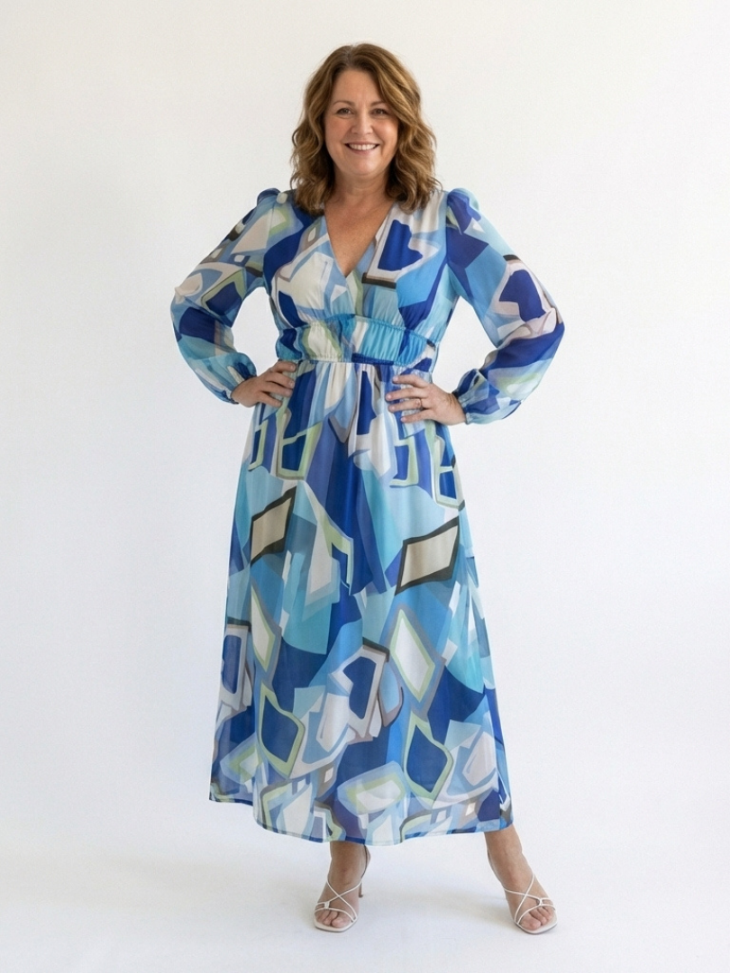 Woman showcasing a flowing floral long sleeve maxi dress on a plain background.