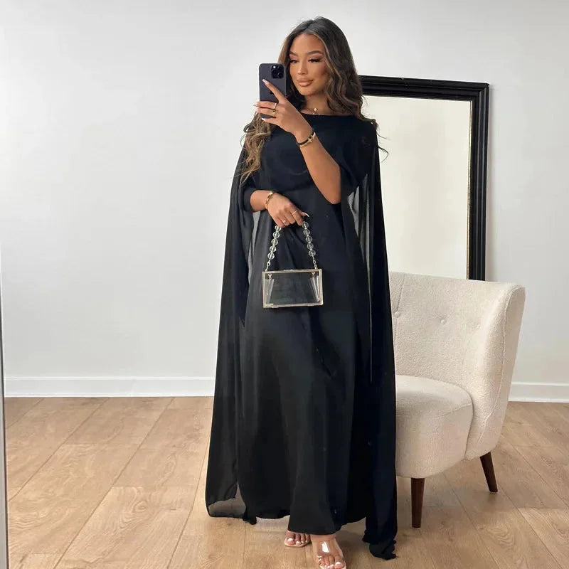 Female model showcasing a maxi dress with elegant cape detail and full-length design.