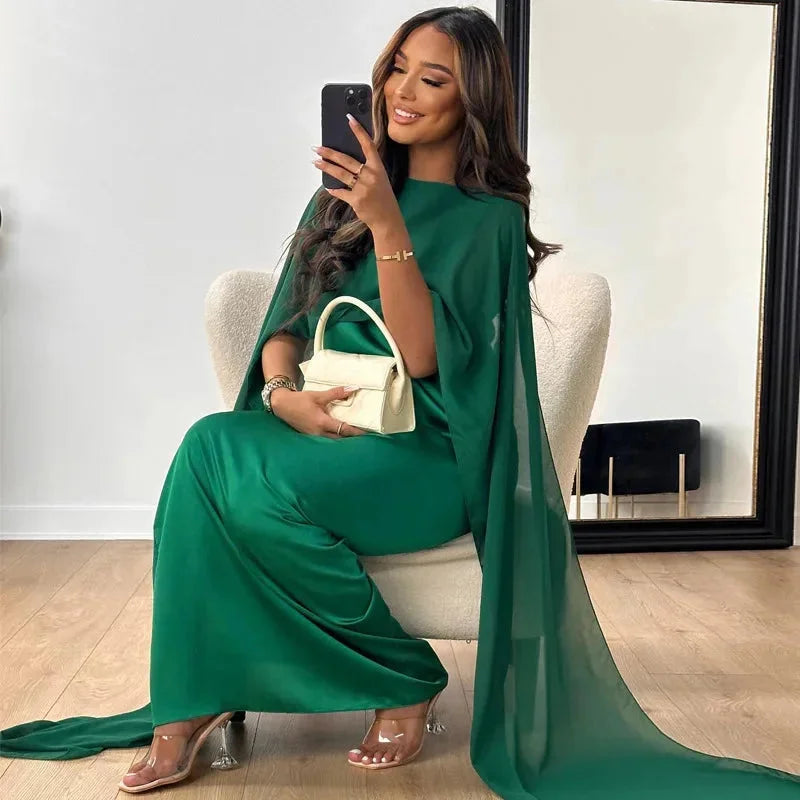 Female model in a long occasion dress with cape sleeves against a plain background.