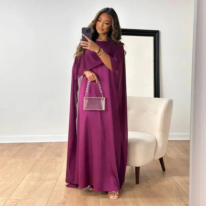 Woman wearing a flowing cape maxi dress suitable for weddings and formal events.
