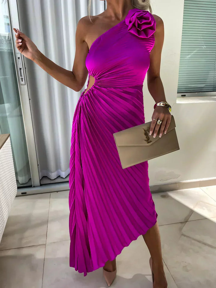 Woman model in an asymmetrical occasion dress with soft structure and floral shoulder accent on a clean background.