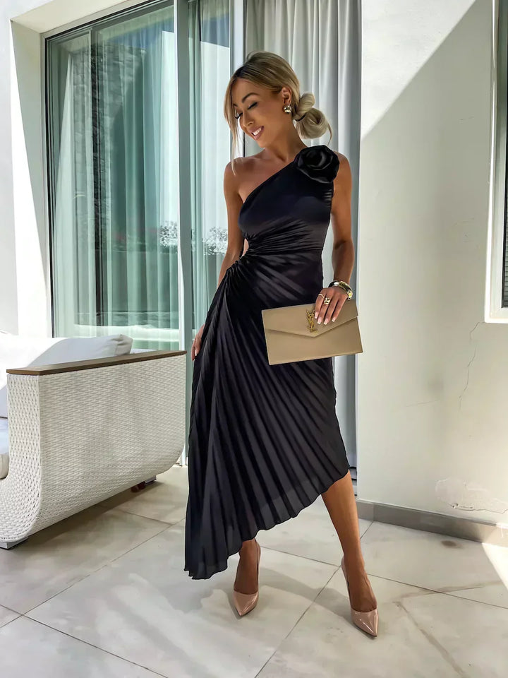 Woman model in a formal one shoulder midi dress with flowing pleated skirt on a plain background