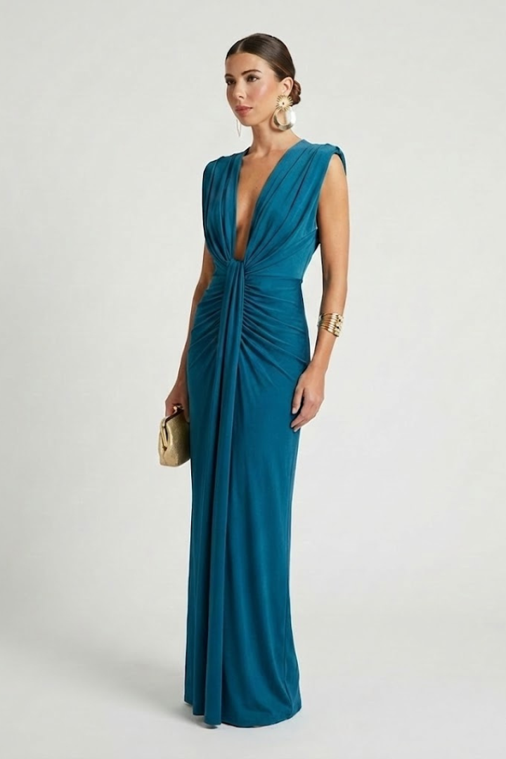 Woman posing in deep V-neck sleeveless green dress against gray background.