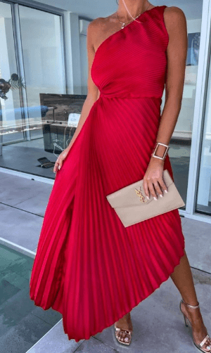 Female model standing in bright lounge wearing pleated evening dress.