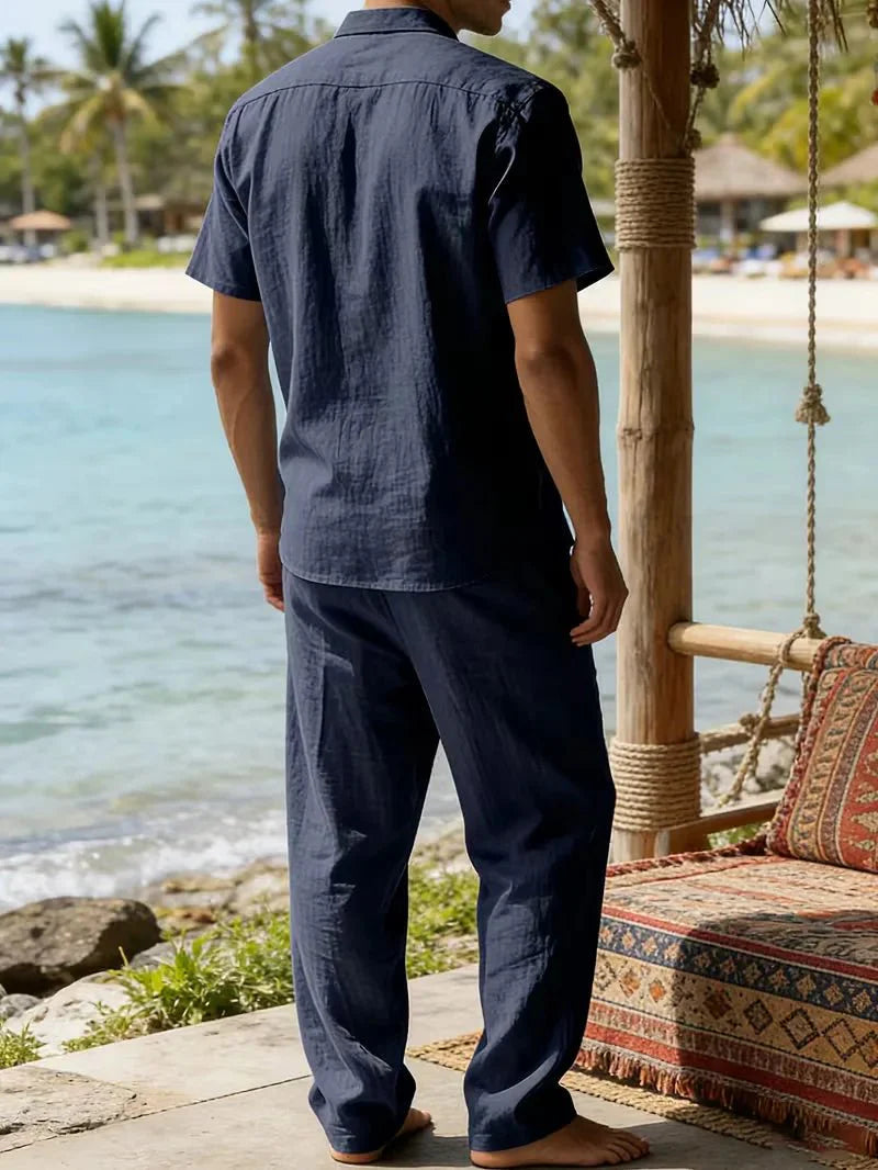  Man wearing a short-sleeve shirt and relaxed trousers on a plain background.