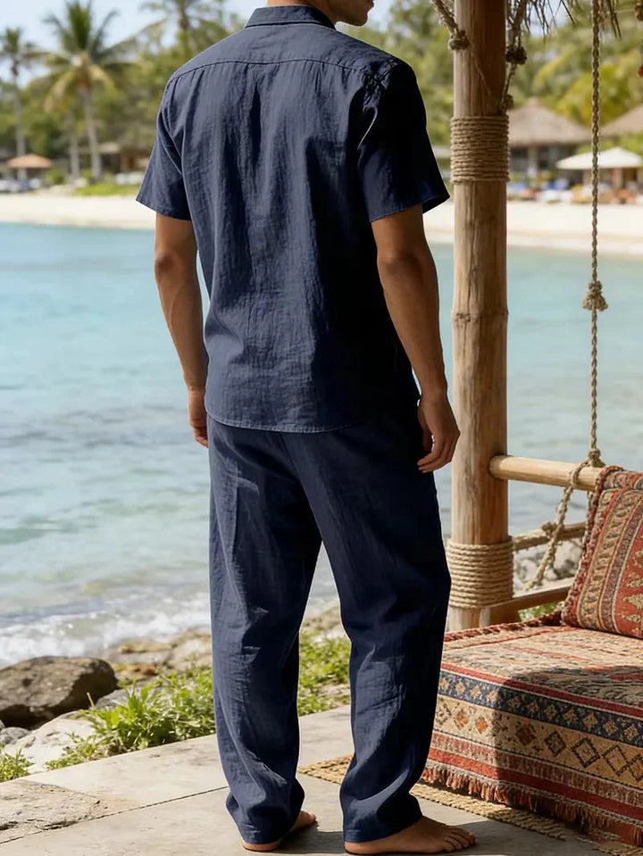  Man wearing a short-sleeve shirt and relaxed trousers on a plain background.