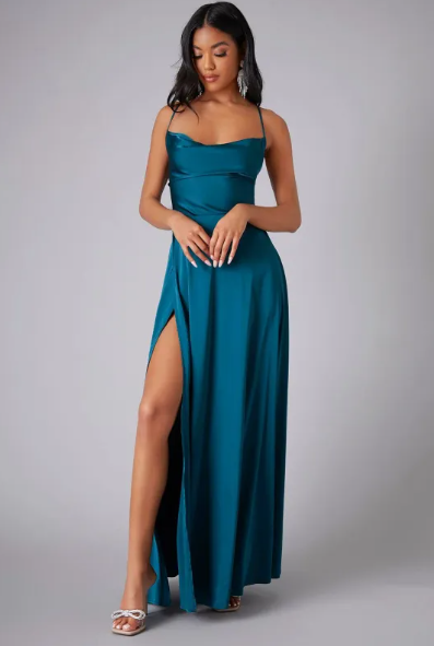 Female wearing a satin cowl neck maxi dress with side slit on a plain background.