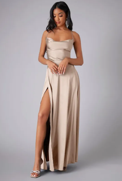 Woman showcasing a satin formal gown with side slit on a plain background.