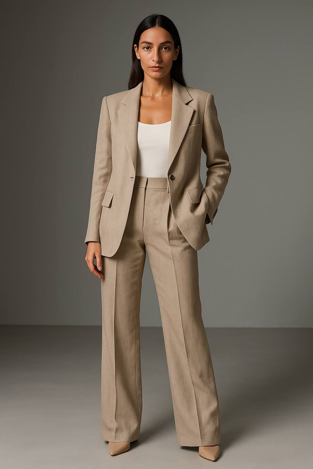 Woman in a structured blazer and wide leg trousers on a plain background.