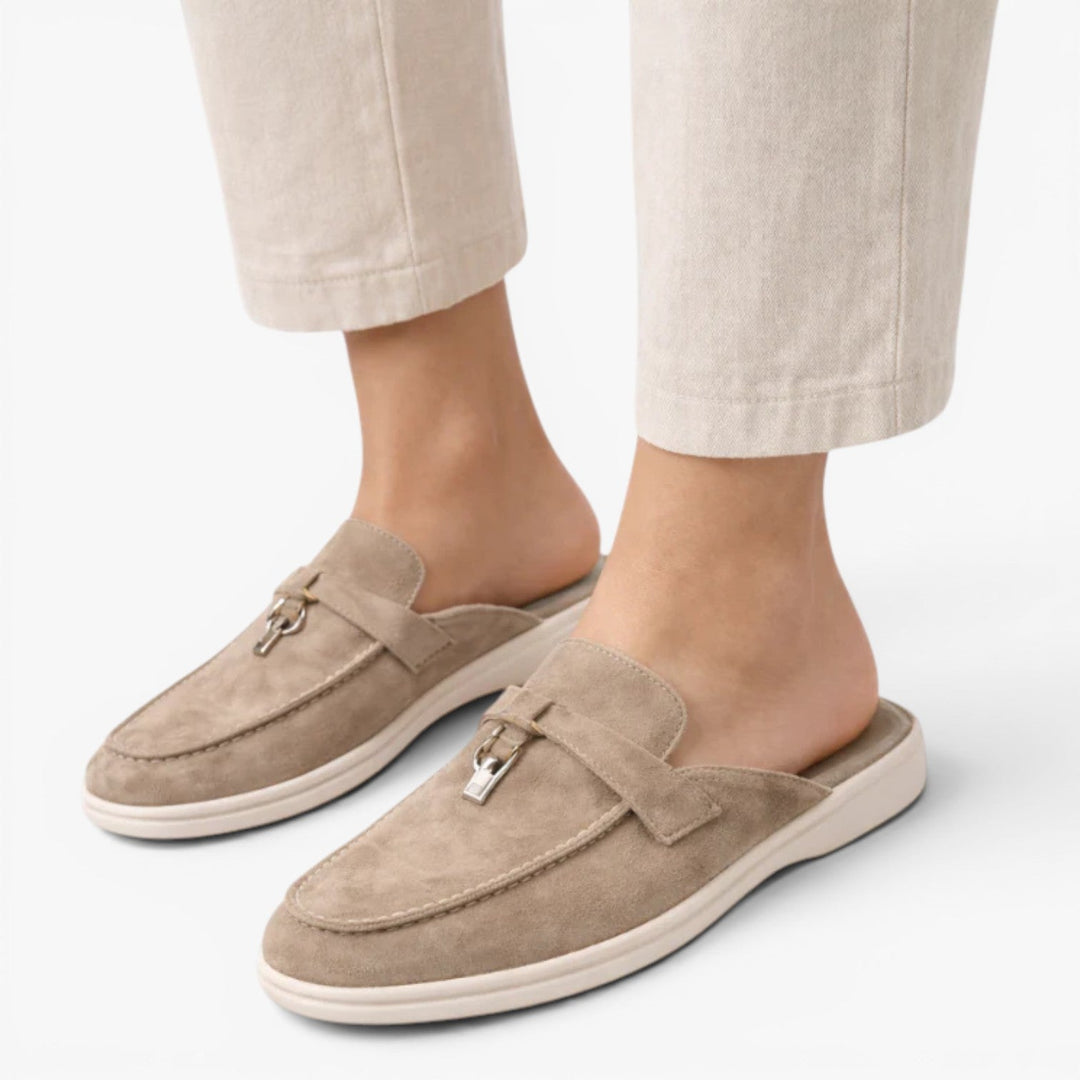 Slip-on mule loafers with almond toe and metal detail on a plain background.