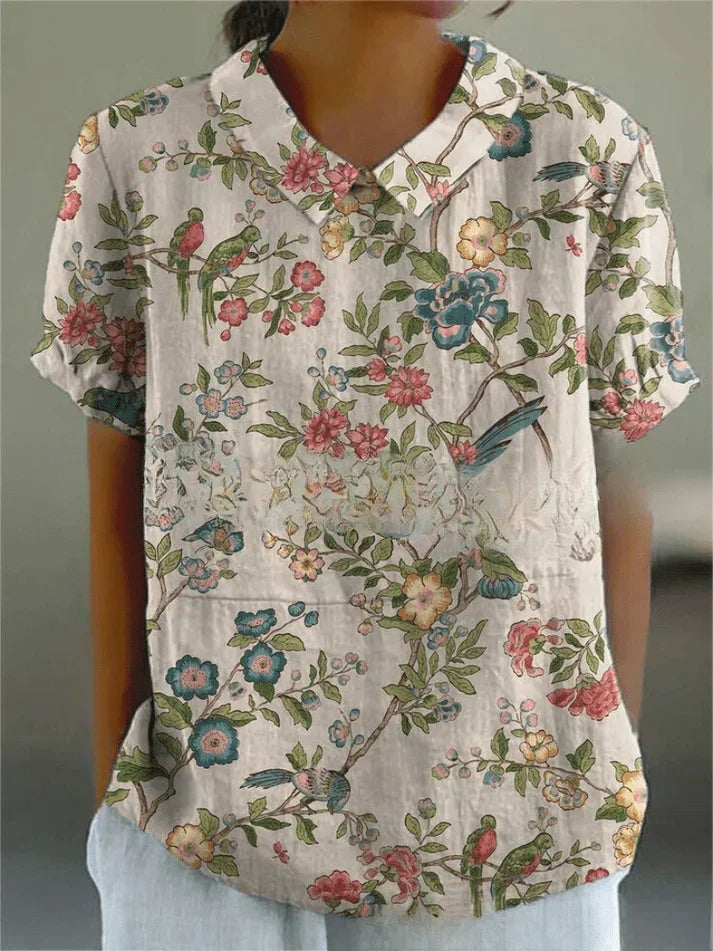 Woman styled in a relaxed floral blouse with a plain background.