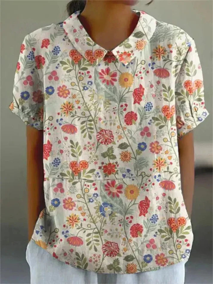 Woman styled in a relaxed floral blouse with a plain background.