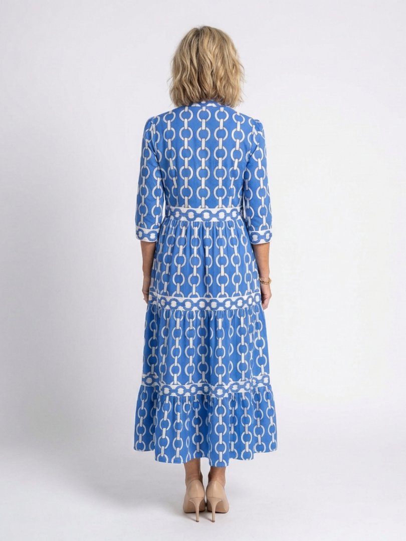 Model in a tiered midi dress with chain pattern and v-neckline on a plain background.