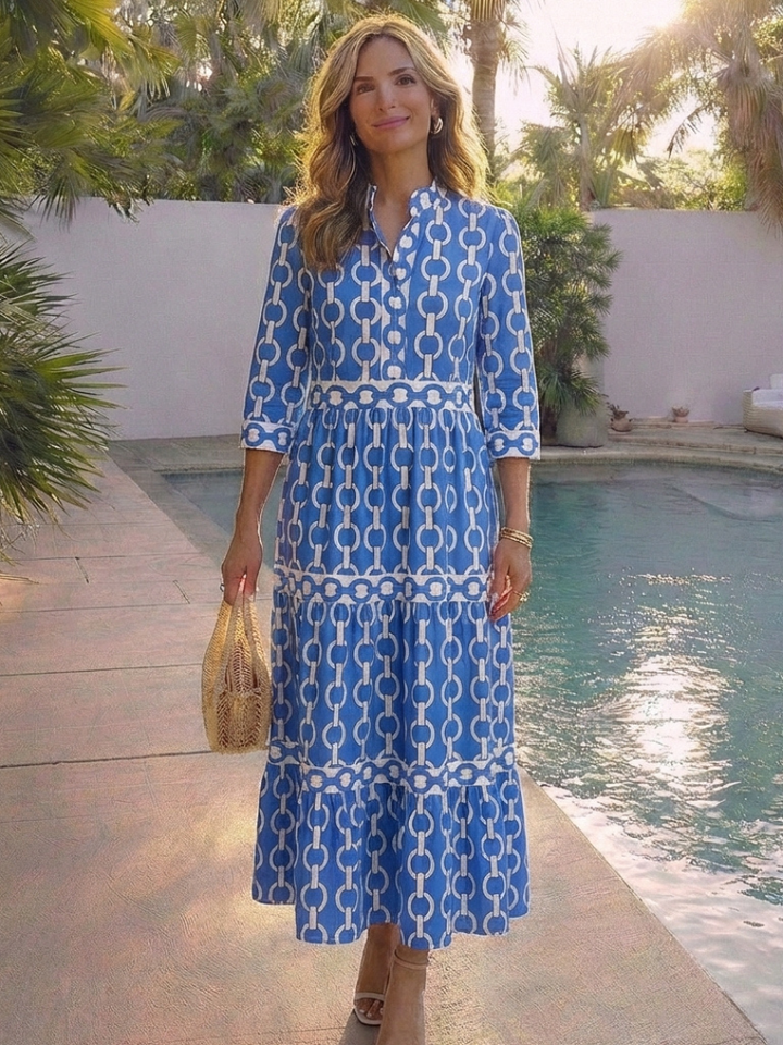 Female wearing a patterned midi dress with layered skirt and plain background.