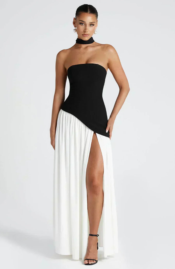 Woman wearing a modern asymmetric maxi dress on a clean plain background.
