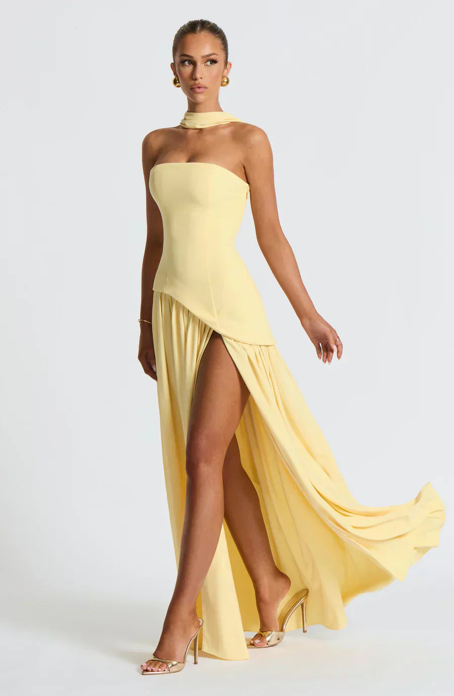 Female model wearing an asymmetric maxi dress on a plain background.
