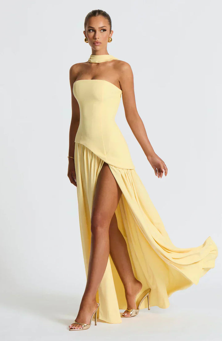 Female model wearing an asymmetric maxi dress on a plain background.
