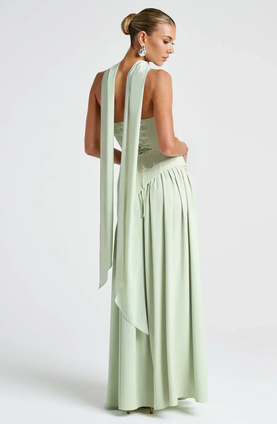 Model standing in formal event dress against plain background, backview