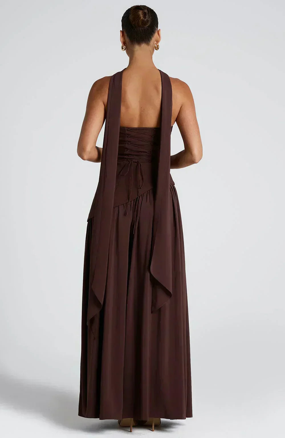 Female model showcasing a modern occasion dress against a simple plain background.
