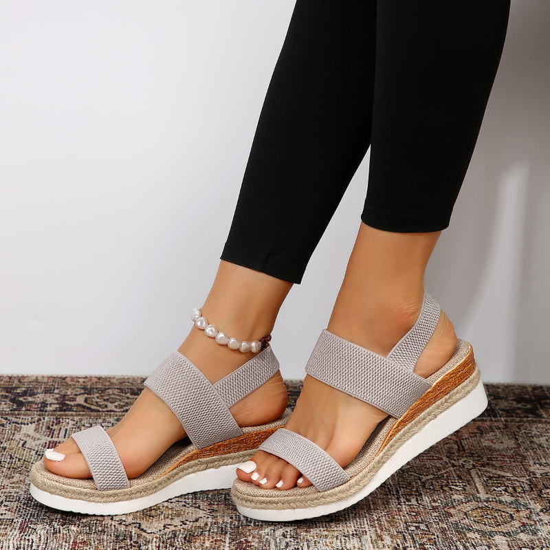 Foot model displaying chic sandals from side on rustic floor.