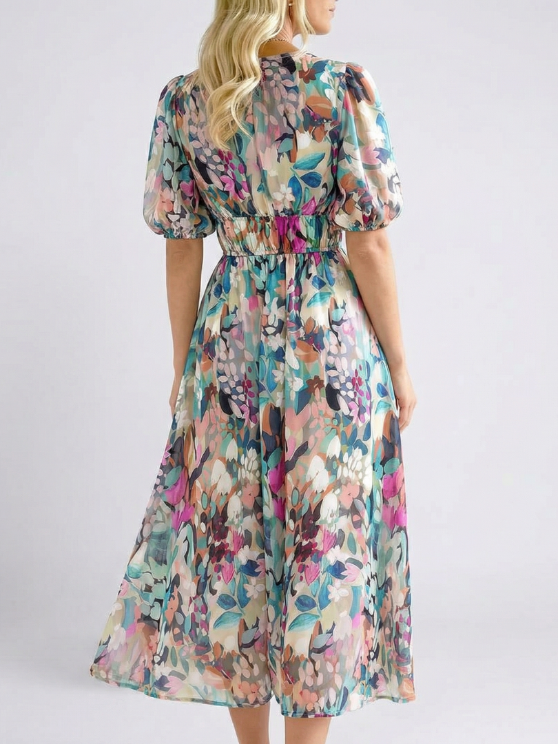 Woman posing in a floral midi dress with gathered waist on a plain backdrop.