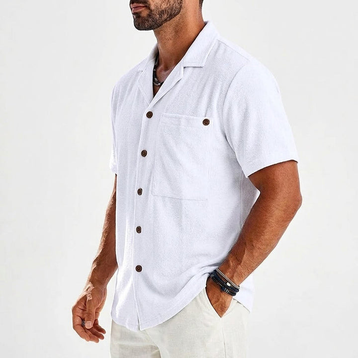  Male model wearing a resort inspired button shirt on a plain background.