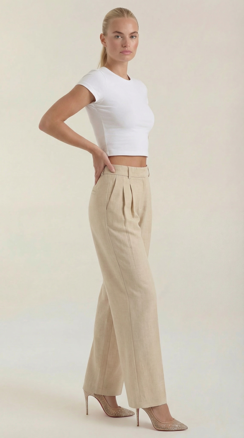 Female model posing in high-waist trousers full body plain background.