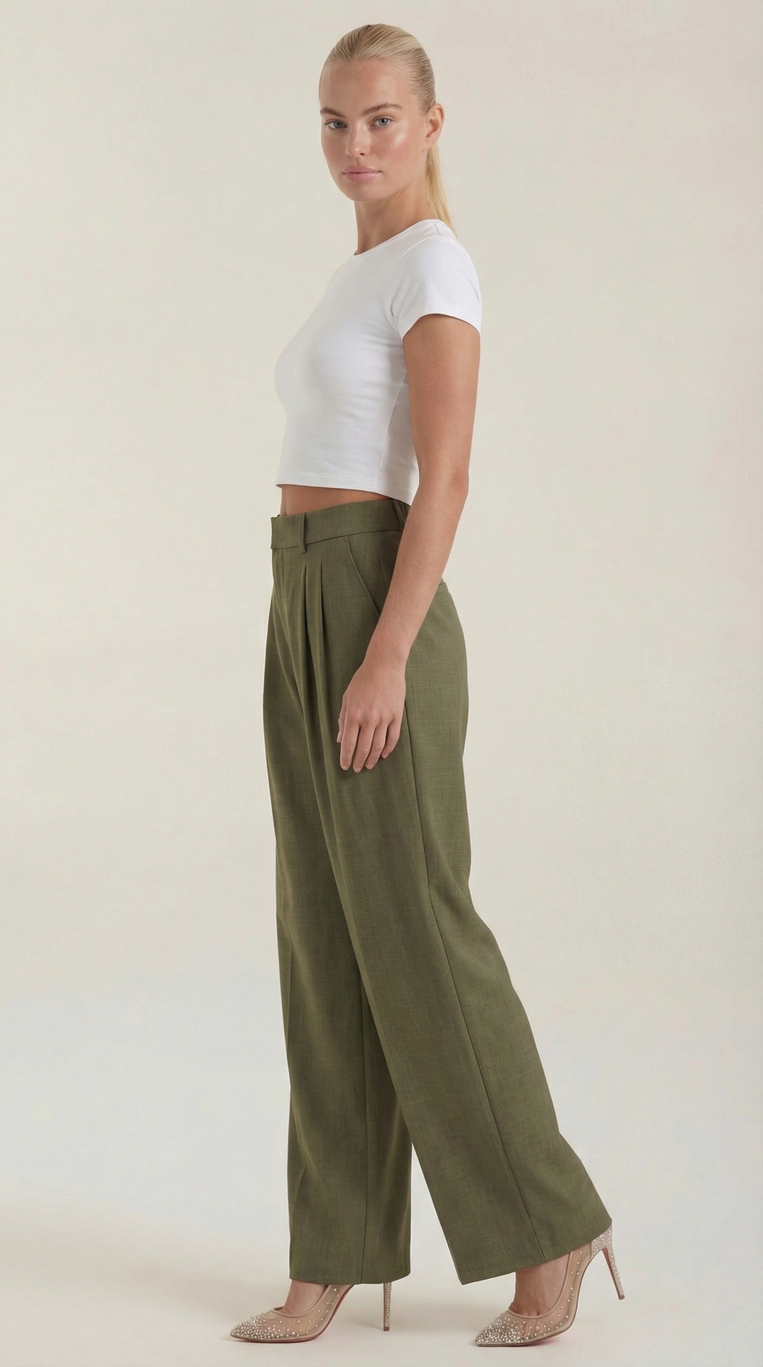 Woman displaying full-length pleated trousers front angle plain background.